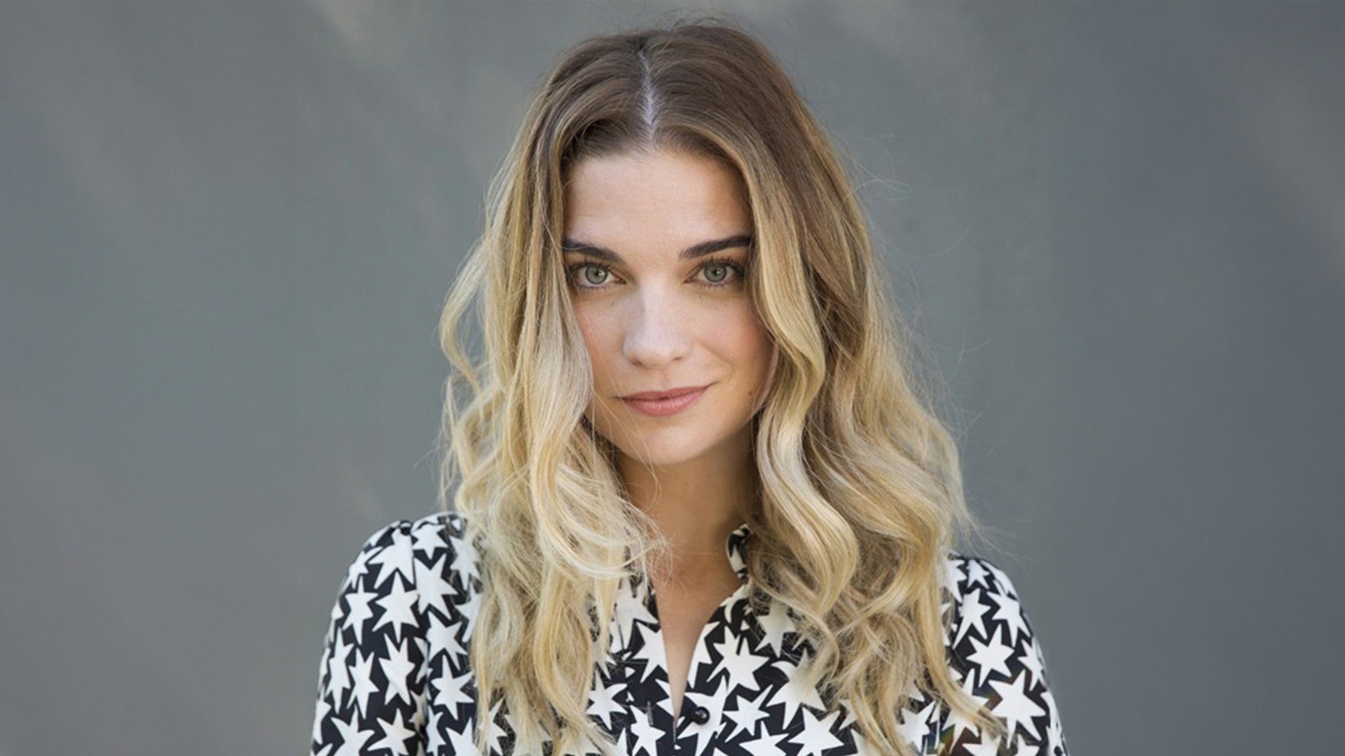 Annie Murphy, BFA 10 Headshot of a woman with blonde wavy hair who wearing a black and white patterned shirt as she stands in front of grey background